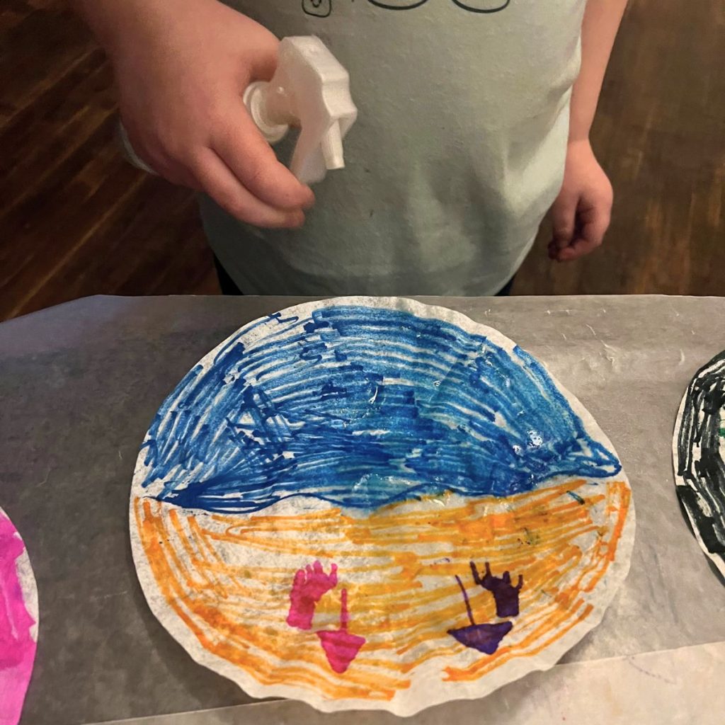 kid spraying water on a coffee filter colored with washable markers