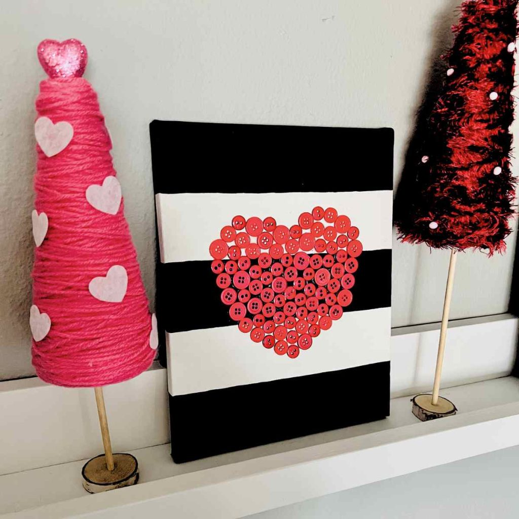 black and white painted wall art canvas with red buttons in the shape of a heart next to valentine red and pink trees