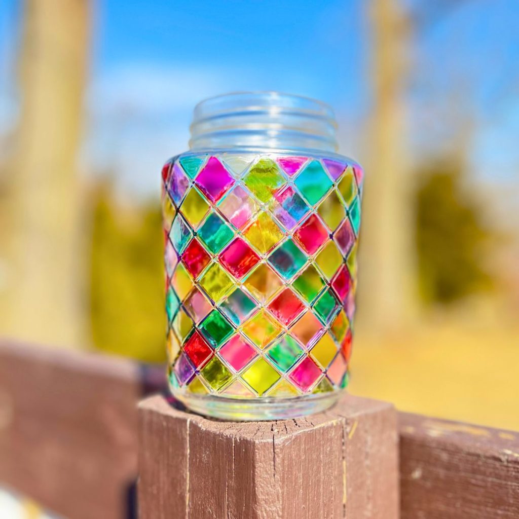 stained glass mason jar outside on brown wood deck in sunlight