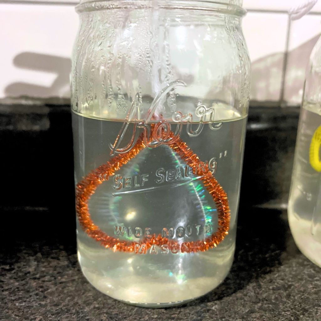 Borax water in mason jar with orange and sparkle pipe cleaner hearts.