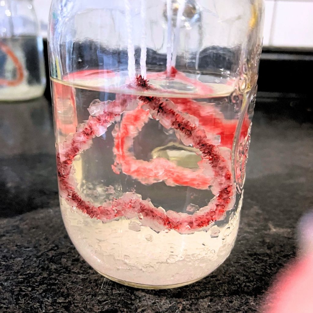 Borax crystals on red pipe cleaner heart in mason jar on black counter