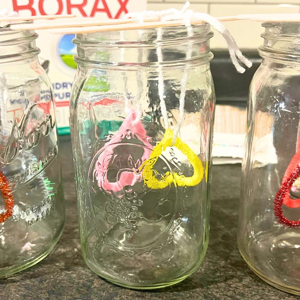 Mason jar with pipe cleaner pink and yellow hearts held by popsicle sticks