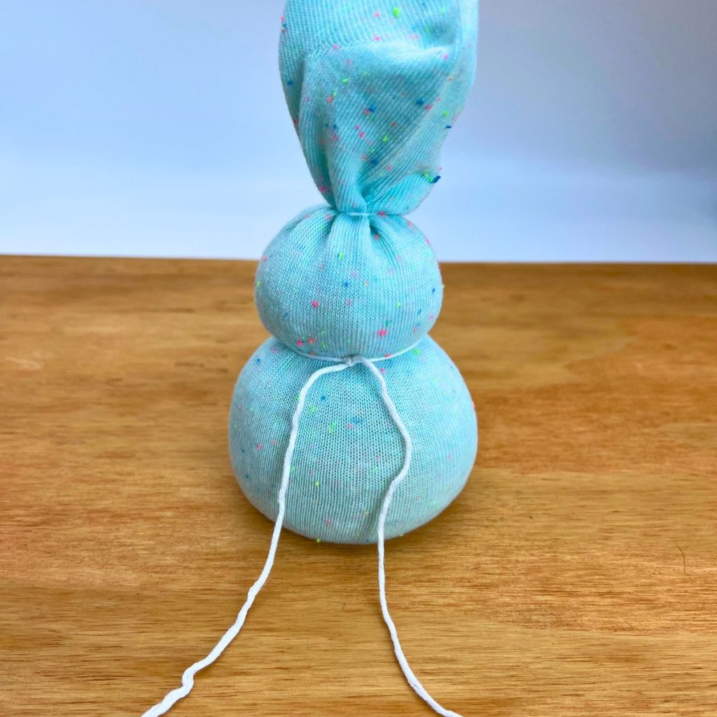 Bunny shape out of a blue sock filled with rice tied with white yarn